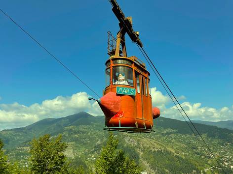 schwebende rostrote Gondel einer Seilbahn mit grünen Berg im Hintergrund