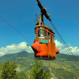 schwebende rostrote Gondel einer Seilbahn mit grünen Berg im Hintergrund